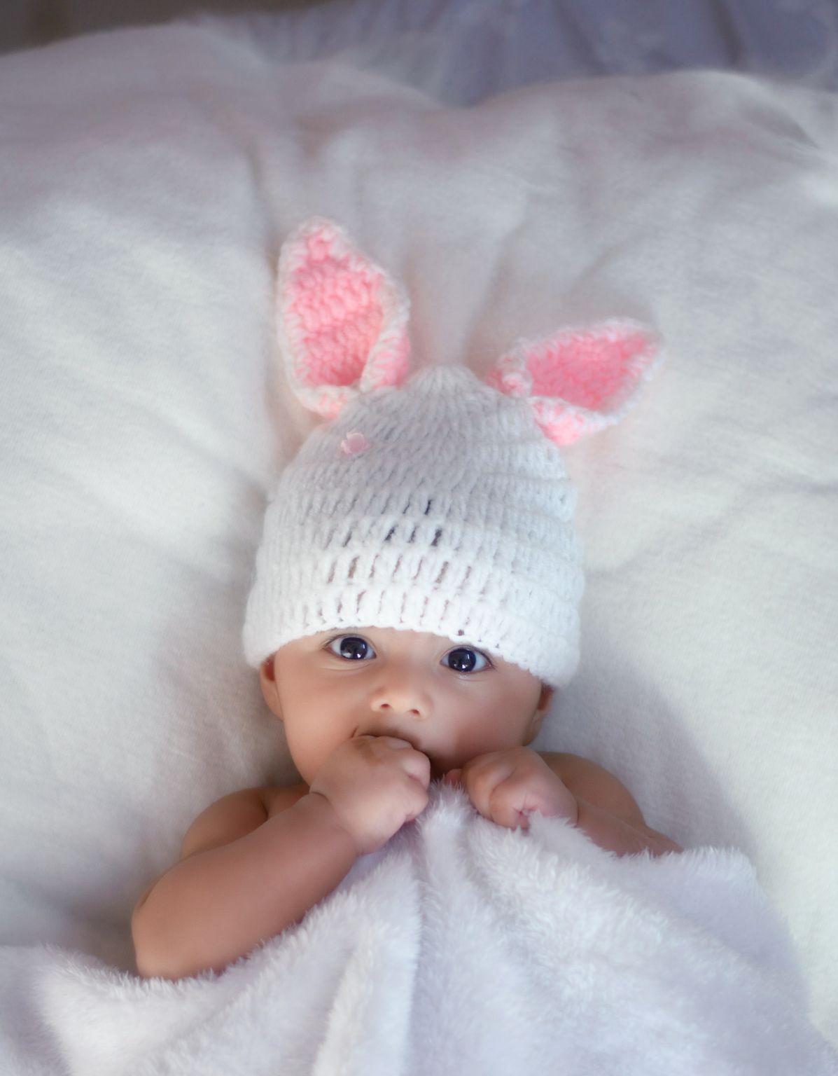 baby in white knit cap lying on white textile
