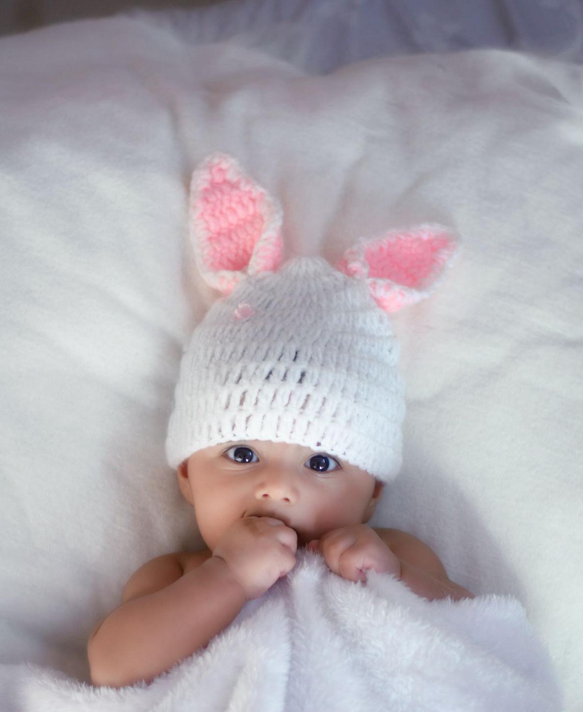 baby in white knit cap lying on white textile